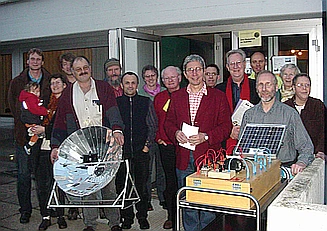 Eine Gruppe Personen während einer Mitgliederversammlung in Regensburg. Ein Solarkocher und der visualisierte Aufbau einer PV-Anlage bilden den Vordergrund. Der Link führt zum ausführlichen Artikel
